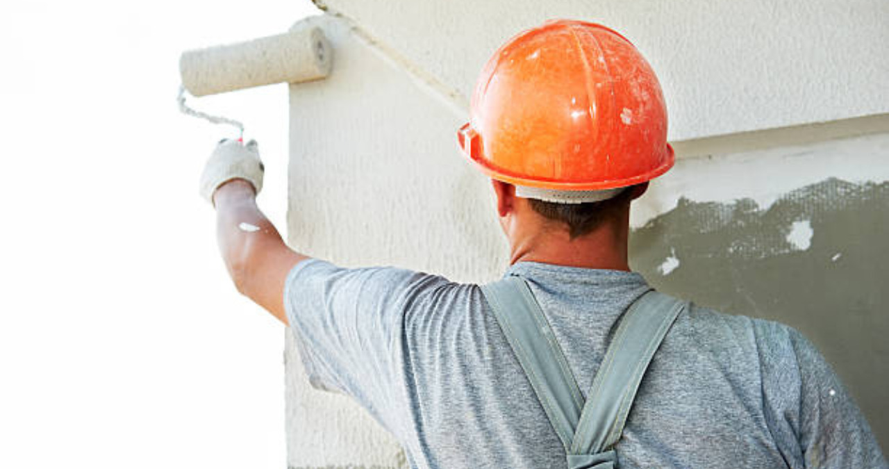 Professional painter performing commercial painting on an exterior wall with a roller.