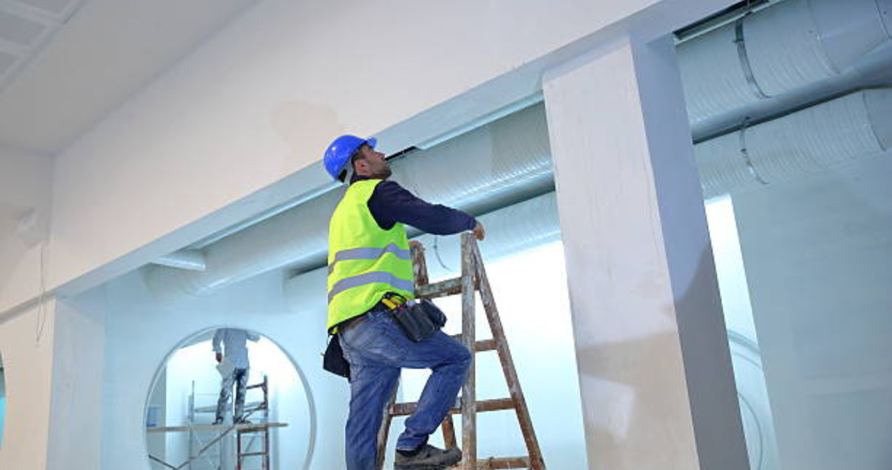 Worker on a ladder applying commercial painting to interior walls of a modern building